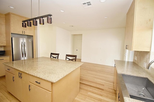 kitchen featuring a kitchen island, stainless steel refrigerator, decorative backsplash, light brown cabinets, and light hardwood / wood-style flooring