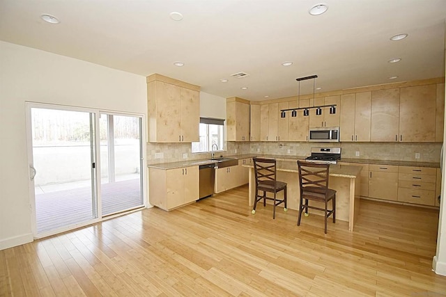 kitchen with hanging light fixtures, light brown cabinets, appliances with stainless steel finishes, a kitchen breakfast bar, and a kitchen island