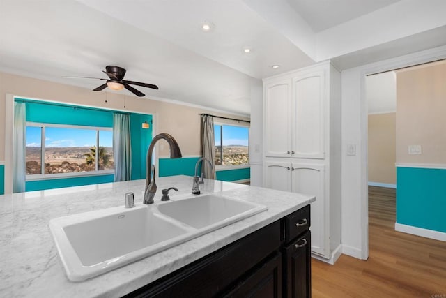 kitchen featuring sink, light stone counters, light wood-type flooring, ceiling fan, and white cabinets