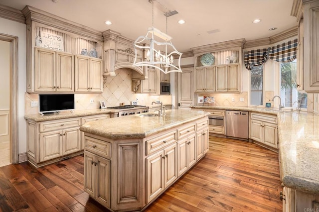 kitchen with sink, hanging light fixtures, an island with sink, stainless steel appliances, and light stone countertops