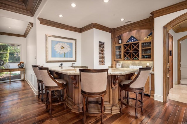 bar featuring ornamental molding, backsplash, dark wood-type flooring, and light stone countertops