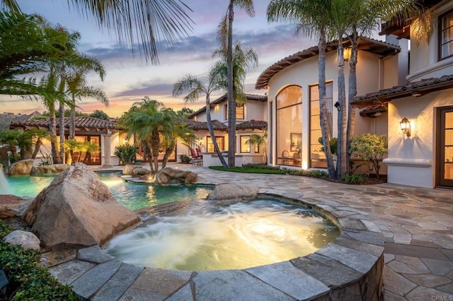 pool at dusk with a patio and an in ground hot tub