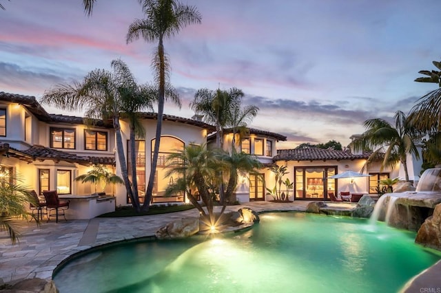 pool at dusk featuring a patio, exterior bar, and a water slide