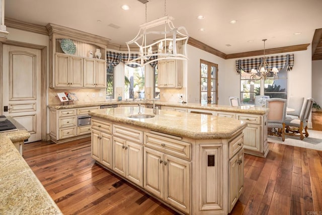 kitchen featuring sink, hanging light fixtures, a notable chandelier, light stone countertops, and a center island with sink