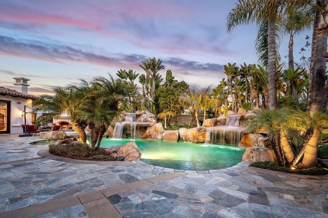 pool at dusk with pool water feature and a patio area