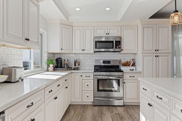 kitchen featuring crown molding, tasteful backsplash, decorative light fixtures, appliances with stainless steel finishes, and light hardwood / wood-style floors