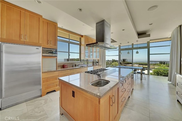 kitchen with tasteful backsplash, island exhaust hood, stainless steel appliances, light stone countertops, and a kitchen island with sink