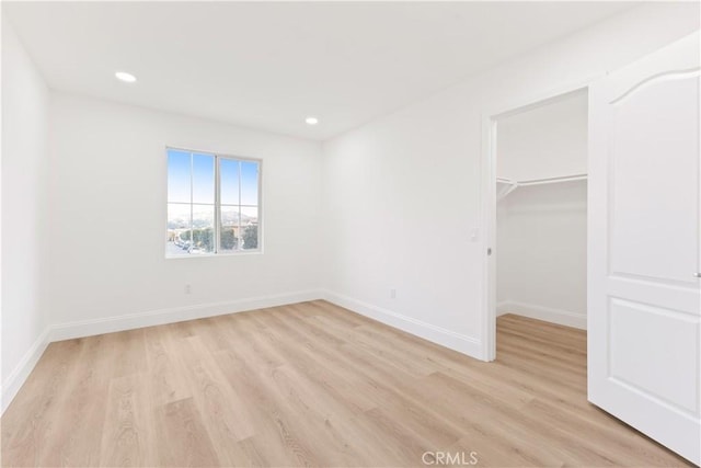 unfurnished bedroom featuring a walk in closet, a closet, and light wood-type flooring