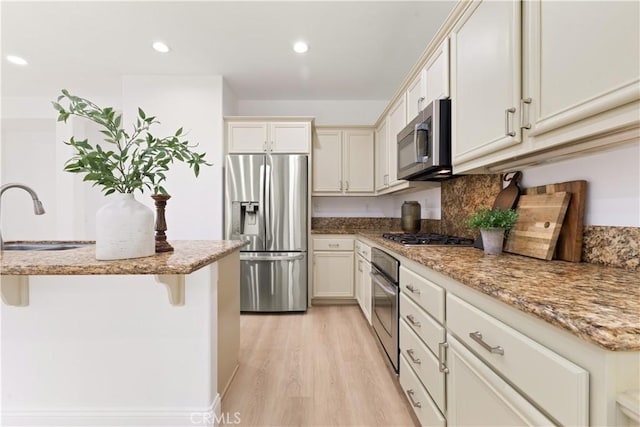 kitchen with sink, light hardwood / wood-style flooring, a breakfast bar, appliances with stainless steel finishes, and light stone counters