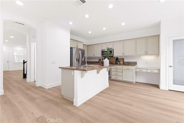 kitchen with a breakfast bar, appliances with stainless steel finishes, dark stone countertops, light hardwood / wood-style floors, and a center island with sink