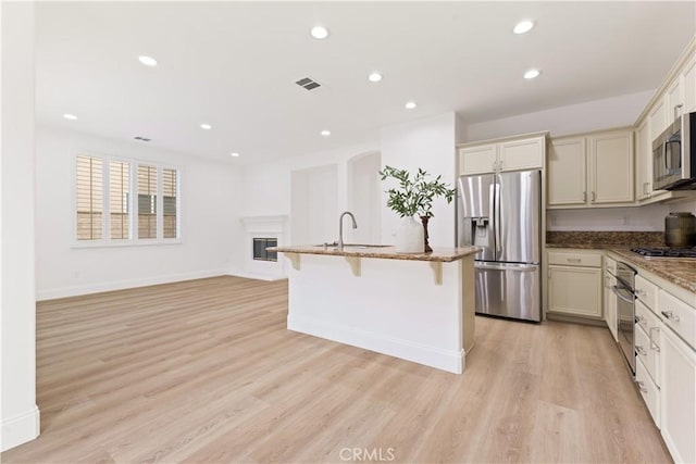 kitchen featuring sink, a breakfast bar area, appliances with stainless steel finishes, light hardwood / wood-style floors, and stone countertops