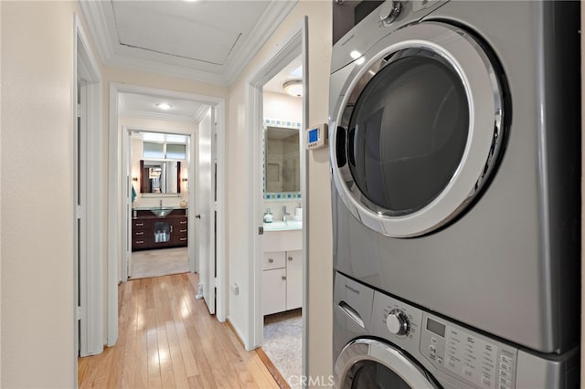 washroom with crown molding, stacked washer and clothes dryer, and light hardwood / wood-style flooring