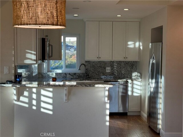 kitchen featuring white cabinetry, appliances with stainless steel finishes, a kitchen breakfast bar, and dark stone counters