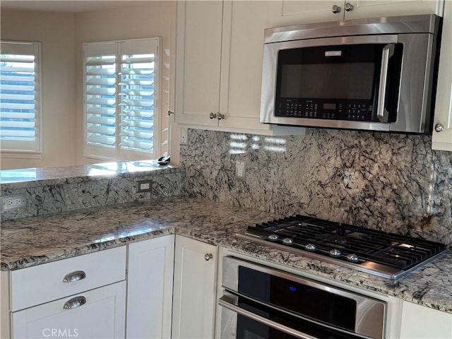 kitchen featuring stainless steel appliances, tasteful backsplash, white cabinetry, and light stone counters