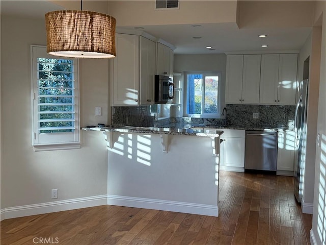 kitchen featuring stone countertops, visible vents, appliances with stainless steel finishes, wood finished floors, and a peninsula