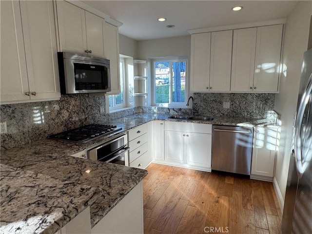 kitchen with light stone countertops, light wood-style floors, stainless steel appliances, and a sink