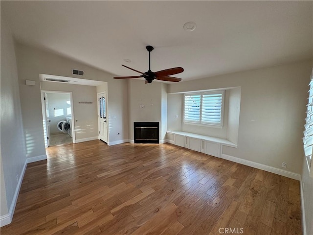 unfurnished living room featuring wood finished floors, a glass covered fireplace, visible vents, and baseboards