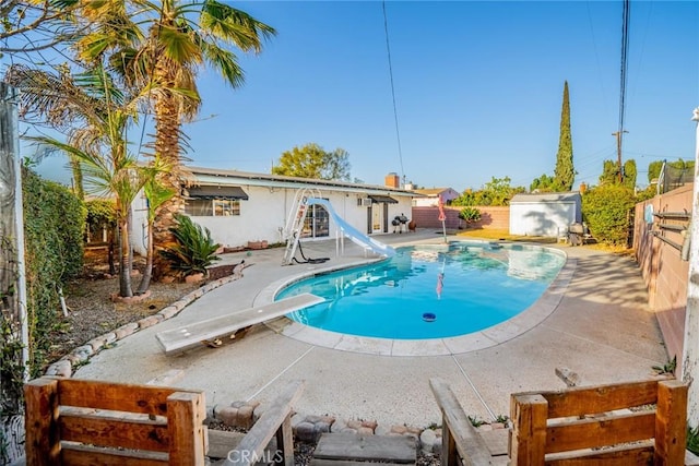 view of swimming pool with a water slide, a diving board, and a patio area