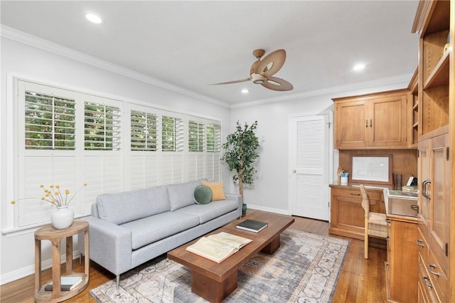 living room featuring ceiling fan, ornamental molding, built in desk, and wood-type flooring