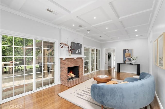 living room with coffered ceiling, beamed ceiling, crown molding, a brick fireplace, and hardwood / wood-style flooring