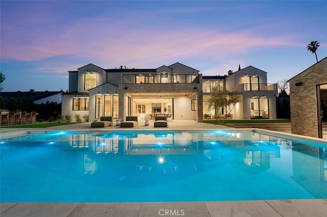 19845 Santa Rita St, Woodland Hills, CA 91364 - back of property at dusk with a patio area, a balcony, outdoor lounge area, an outdoor pool, and stucco siding