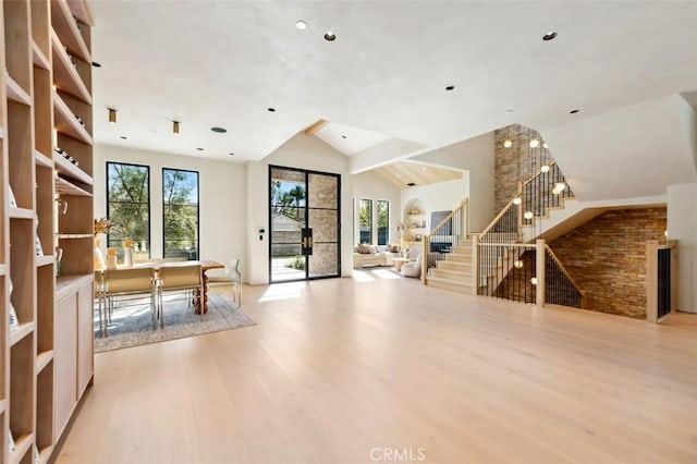 unfurnished living room featuring light wood-style flooring, stairs, and high vaulted ceiling