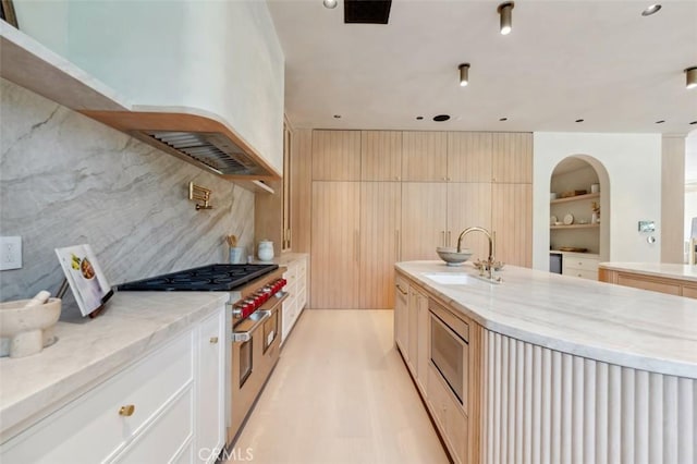 kitchen featuring tasteful backsplash, an island with sink, sink, range with two ovens, and light hardwood / wood-style floors