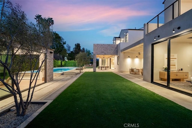 yard at dusk featuring a balcony, a patio area, and an outdoor pool