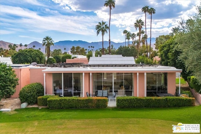 back of property featuring a mountain view, a yard, and a sunroom