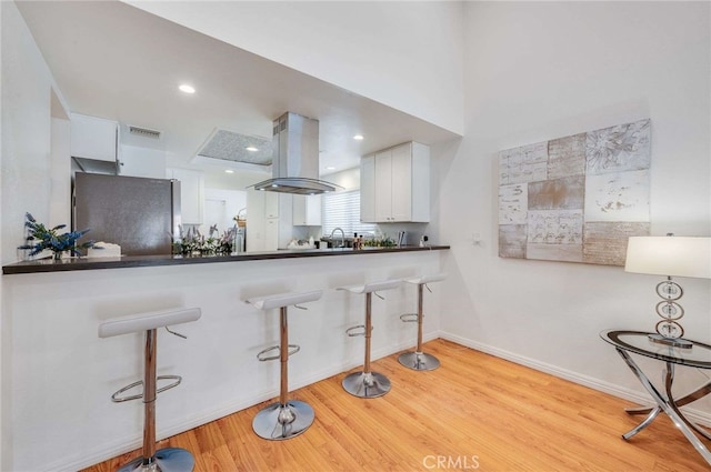 kitchen featuring white cabinetry, light hardwood / wood-style flooring, stainless steel refrigerator, kitchen peninsula, and island exhaust hood