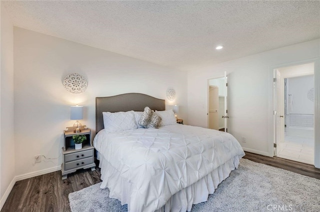 bedroom with a spacious closet, connected bathroom, a textured ceiling, and dark hardwood / wood-style flooring