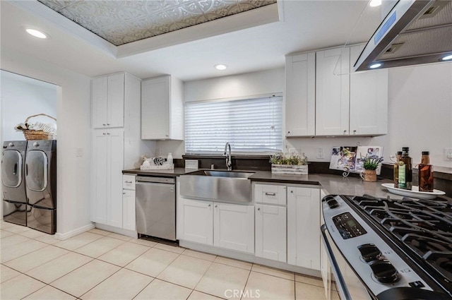 kitchen with a tray ceiling, independent washer and dryer, stainless steel appliances, range hood, and white cabinets