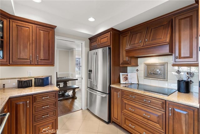 kitchen with backsplash, light tile patterned floors, light stone counters, stainless steel fridge with ice dispenser, and black electric cooktop