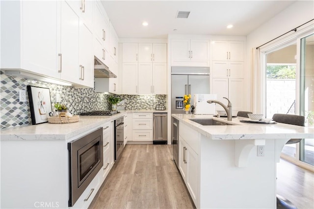 kitchen with sink, appliances with stainless steel finishes, a kitchen breakfast bar, tasteful backsplash, and white cabinets