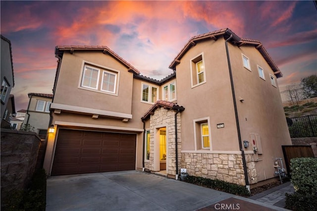 mediterranean / spanish home featuring an attached garage, fence, stone siding, concrete driveway, and stucco siding