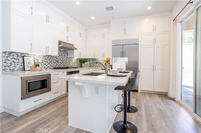 kitchen with built in appliances, a breakfast bar, a center island with sink, and white cabinets