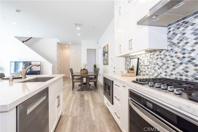 kitchen with white cabinetry, sink, exhaust hood, light hardwood / wood-style floors, and stainless steel appliances