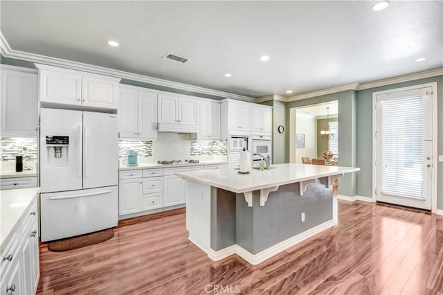 kitchen with white appliances, a kitchen island with sink, white cabinetry, ornamental molding, and light hardwood / wood-style floors