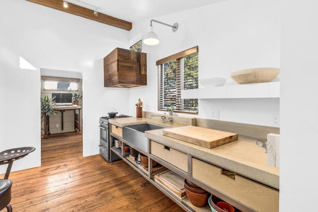 kitchen featuring stainless steel gas stove, beam ceiling, dark wood-type flooring, and rail lighting