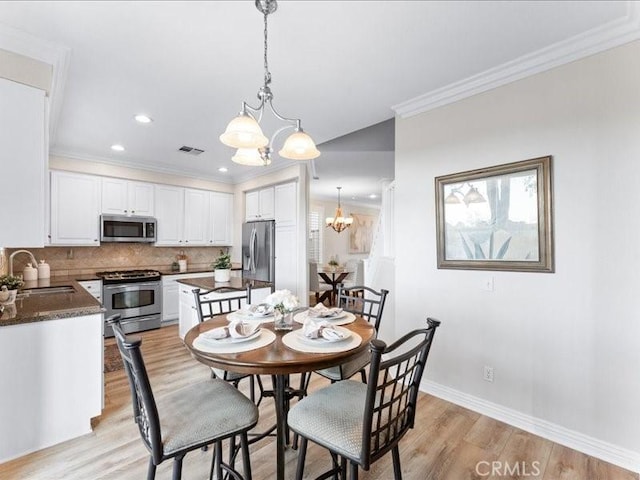 dining room featuring an inviting chandelier, crown molding, light hardwood / wood-style floors, and sink