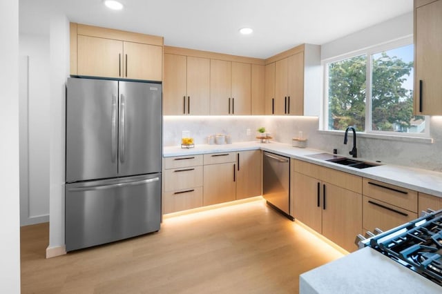 kitchen featuring appliances with stainless steel finishes, tasteful backsplash, sink, light brown cabinets, and light wood-type flooring