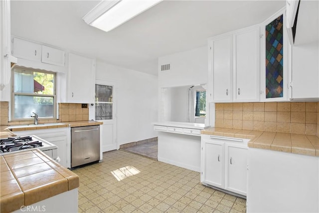 kitchen with tasteful backsplash, tile countertops, range, stainless steel dishwasher, and white cabinets