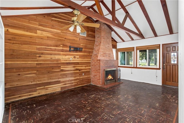 unfurnished living room with ceiling fan, beam ceiling, a brick fireplace, and wood walls