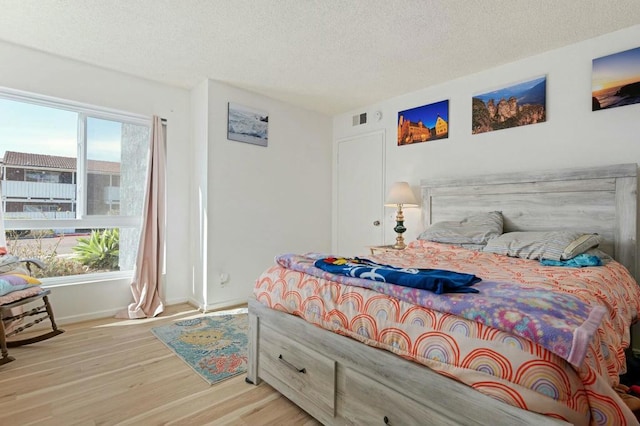 bedroom featuring multiple windows, a textured ceiling, and light hardwood / wood-style floors