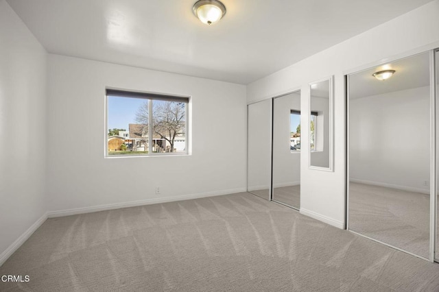 unfurnished bedroom featuring multiple windows, two closets, and light colored carpet