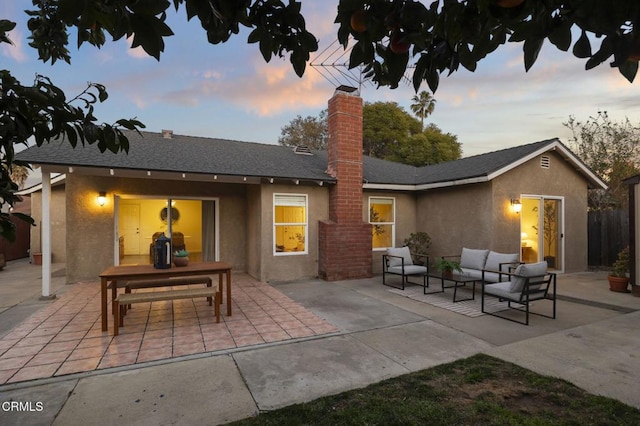 back house at dusk with outdoor lounge area and a patio