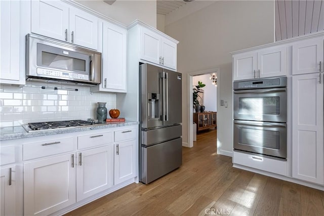 kitchen with light hardwood / wood-style flooring, stainless steel appliances, light stone countertops, white cabinets, and decorative backsplash