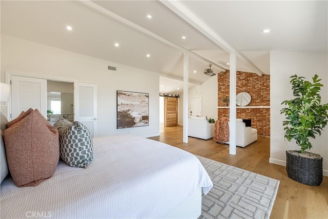 bedroom with light hardwood / wood-style floors, a fireplace, lofted ceiling with beams, and a barn door