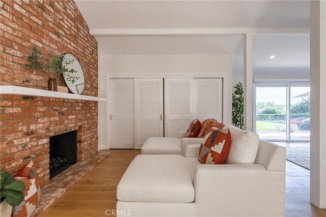 living room featuring brick wall, a fireplace, and light hardwood / wood-style floors