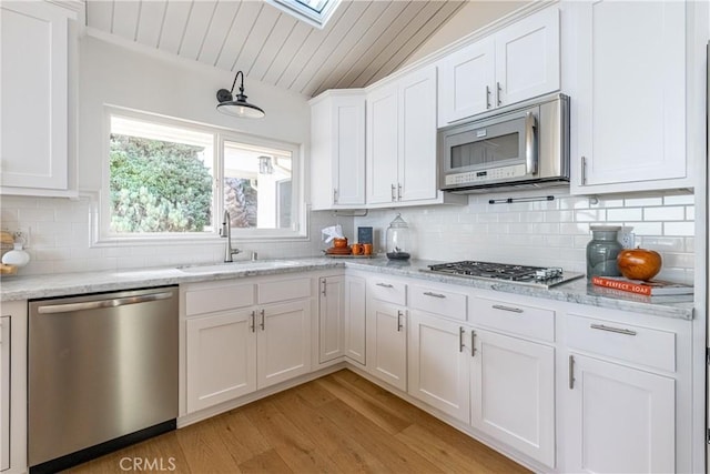 kitchen featuring sink, tasteful backsplash, stainless steel appliances, light stone countertops, and white cabinets